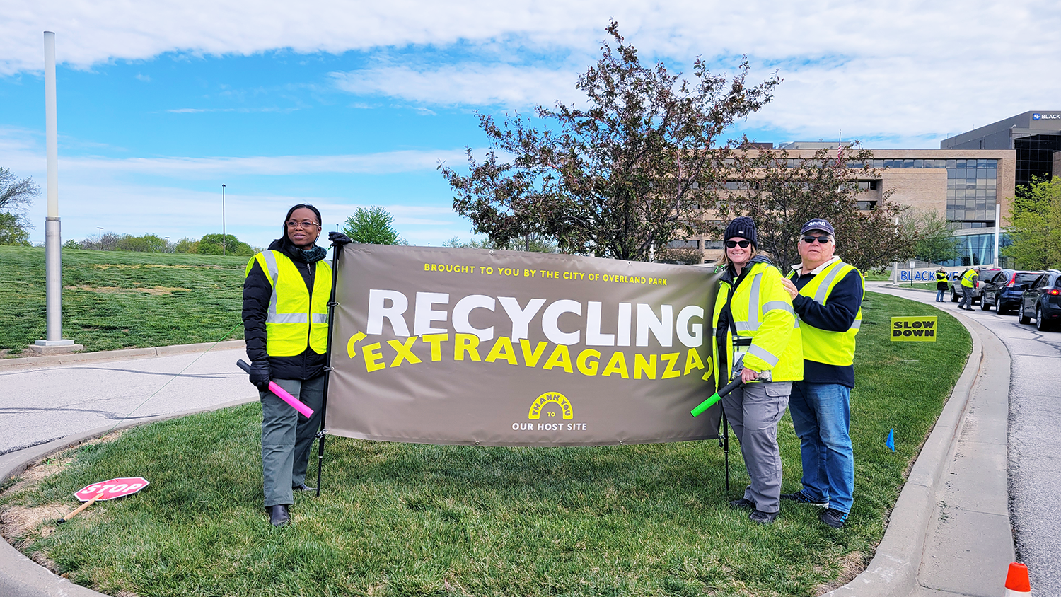 Volunteers stand and smile next to the Recycling Extravaganza banner.