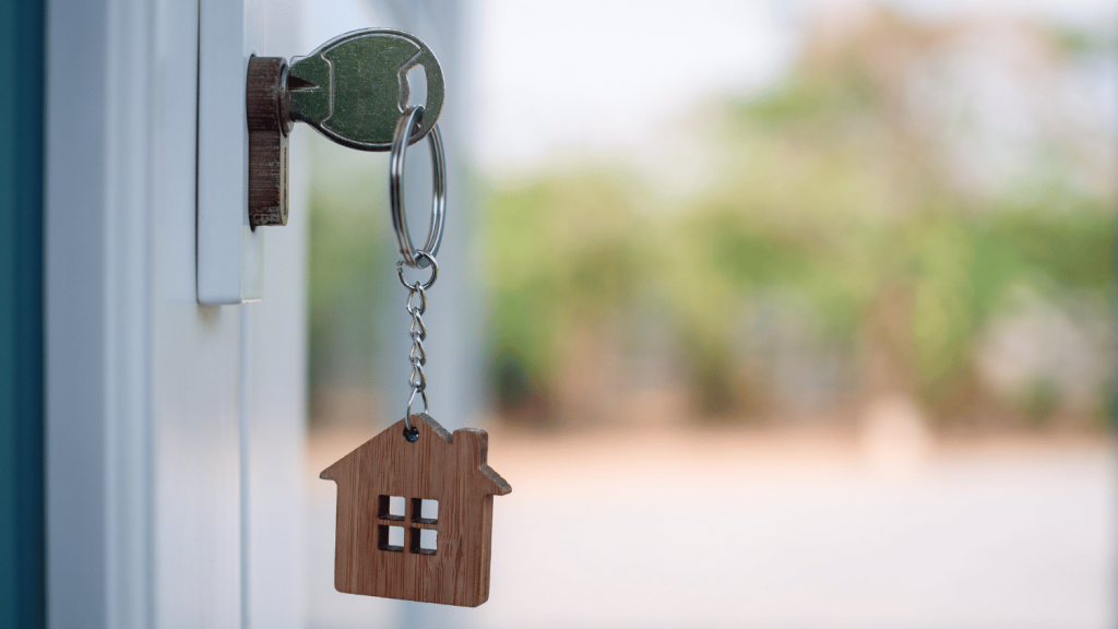 House key on a home-shaped key chain hangs from a door lock.